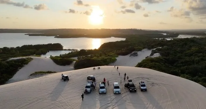 Vários 4x4 no alto da duna no pôr do sol, com a lagoa ao fundo