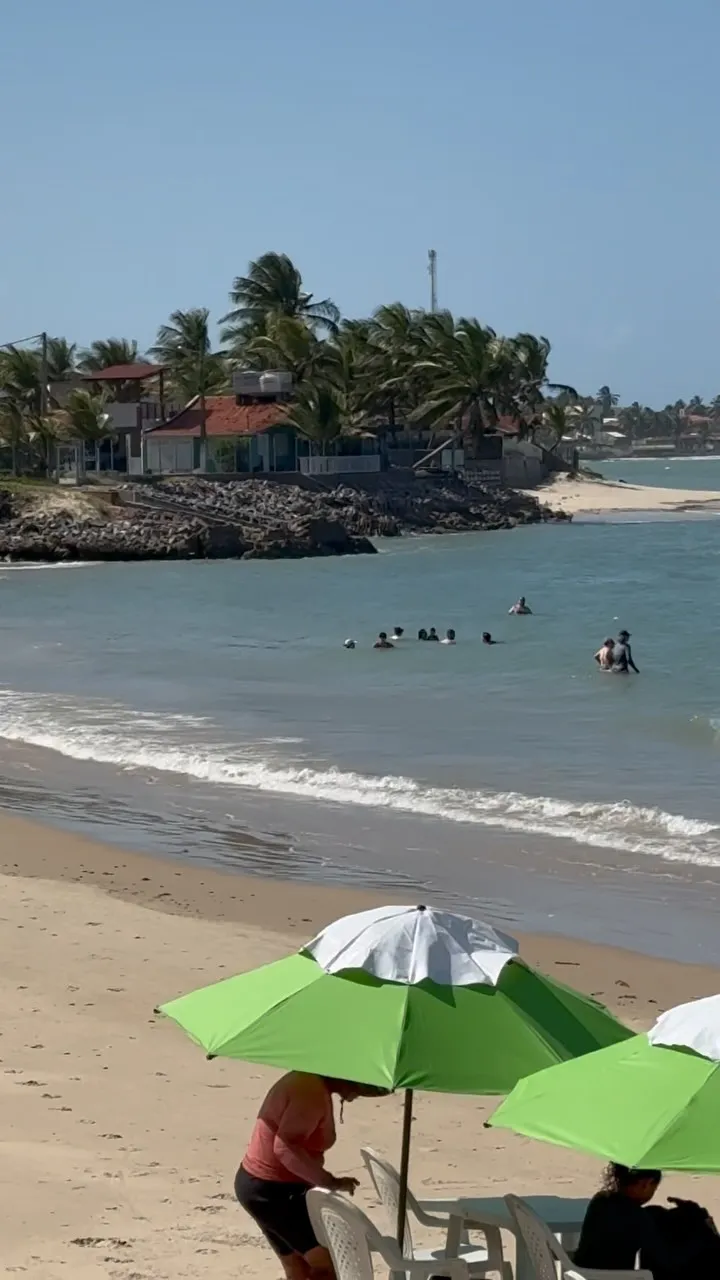 Praia com banhistas no mar e guarda-sóis verdes na areia